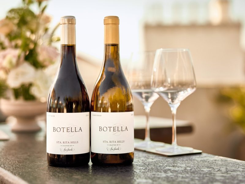 Two bottles of Sea Smoke Botella wine with glasses in the background, set on a dark stone surface.