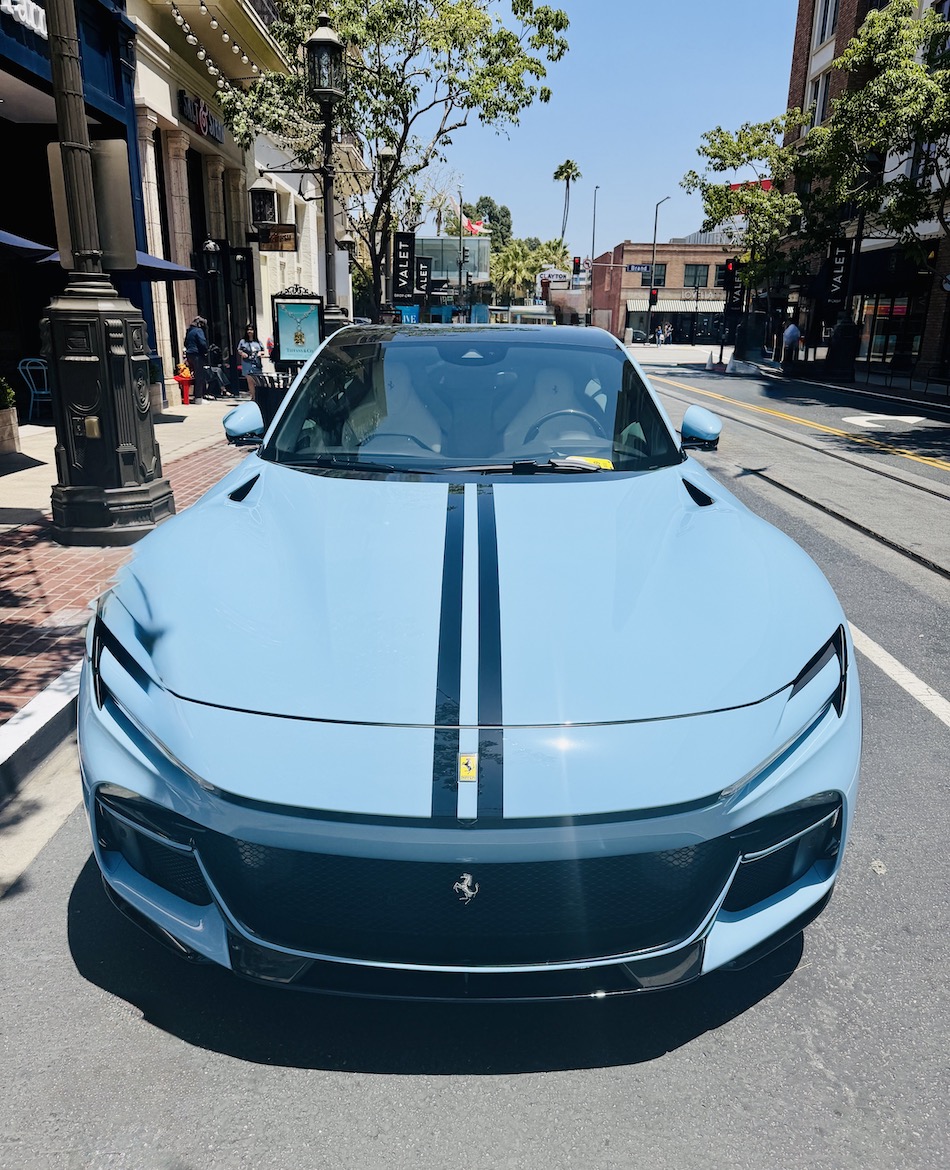 A blue Ferrari Purosangue parked on a city street, showcasing its sleek design and distinctive racing stripes.