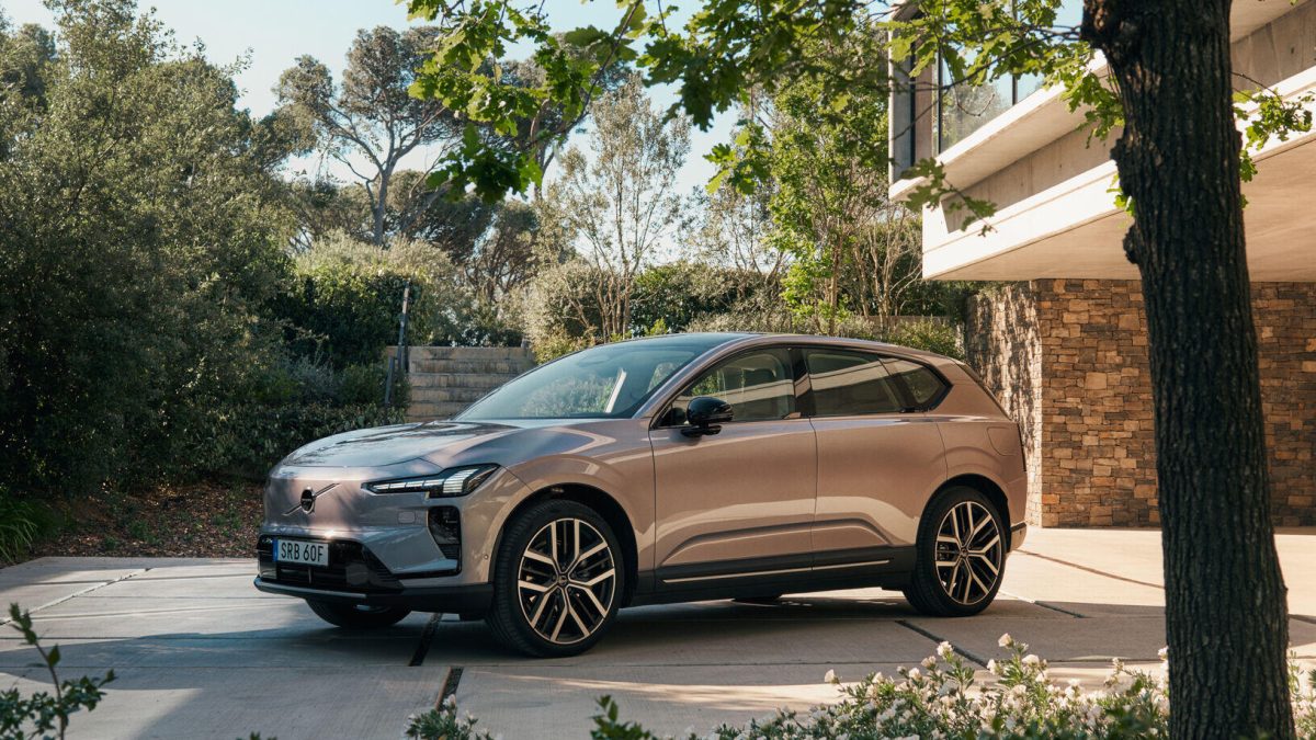 Volvo EX60 parked in a modern outdoor setting, showcasing its sleek design surrounded by greenery and architecture.