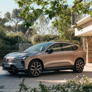 Volvo EX60 parked in a modern outdoor setting, showcasing its sleek design surrounded by greenery and architecture.