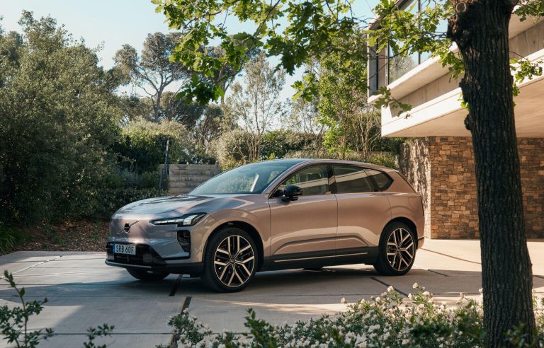 Volvo EX60 parked in a modern outdoor setting, showcasing its sleek design surrounded by greenery and architecture.