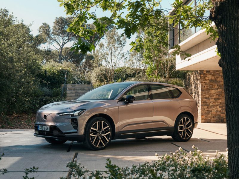Volvo EX60 parked in a modern outdoor setting, showcasing its sleek design surrounded by greenery and architecture.