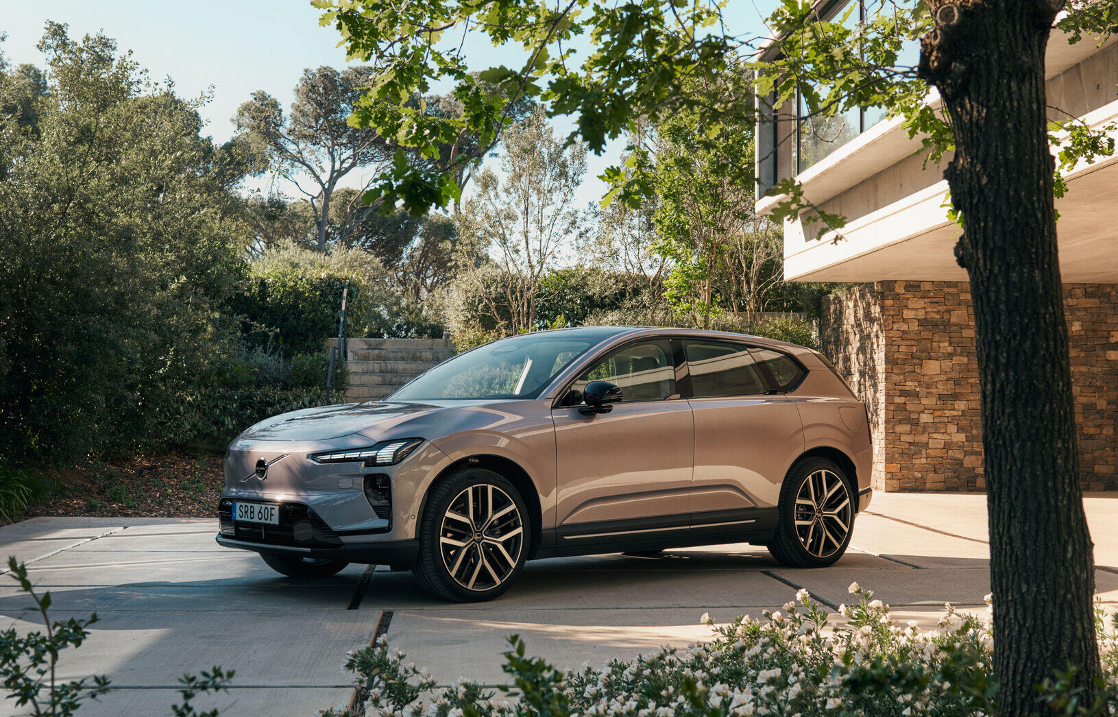 Volvo EX60 parked in a modern outdoor setting, showcasing its sleek design surrounded by greenery and architecture.