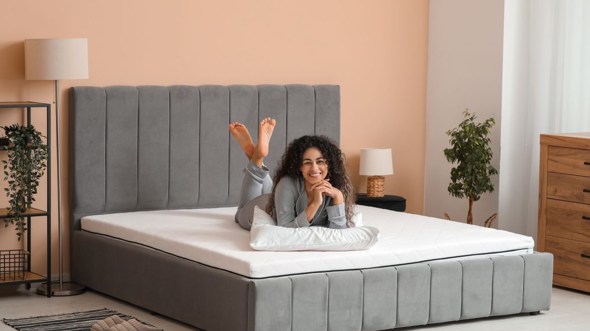 Woman relaxing on a comfortable gray mattress in a stylish bedroom, highlighting sleep quality and comfort.