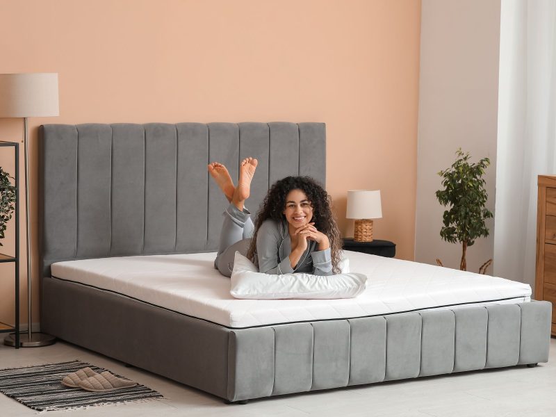 Woman relaxing on a comfortable gray mattress in a stylish bedroom, highlighting sleep quality and comfort.