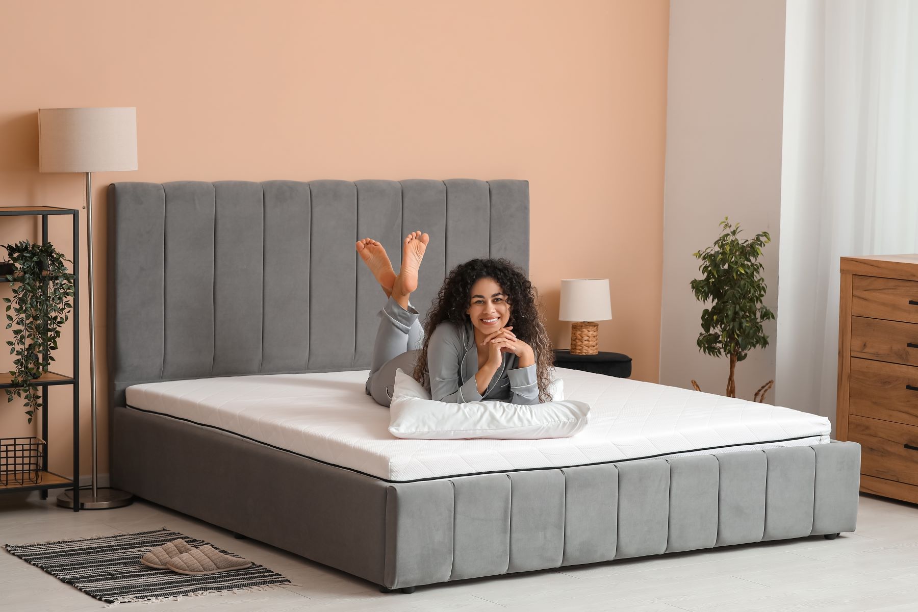 Woman relaxing on a comfortable gray mattress in a stylish bedroom, highlighting sleep quality and comfort.