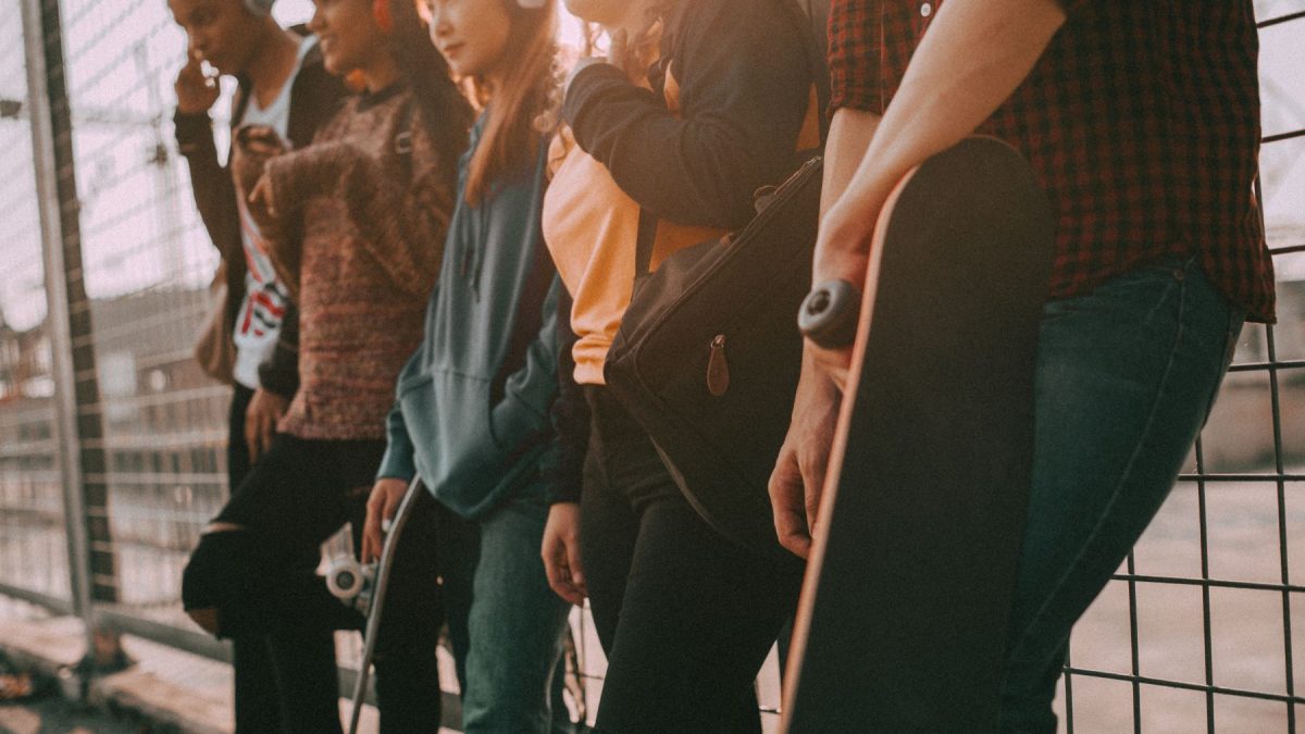 A group of young people wearing headphones stand casually against a fence, showcasing modern street fashion and lifestyle.