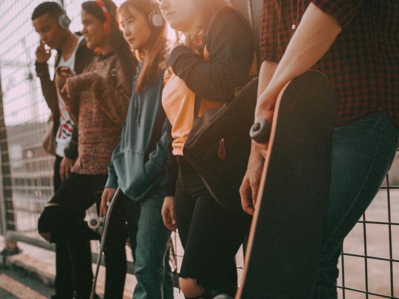 A group of young people wearing headphones stand casually against a fence, showcasing modern street fashion and lifestyle.