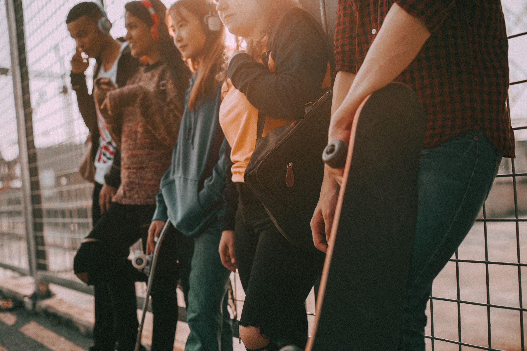A group of young people wearing headphones stand casually against a fence, showcasing modern street fashion and lifestyle.