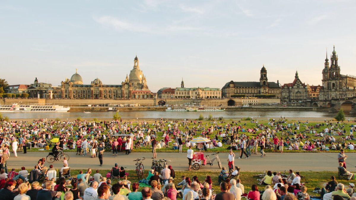 Crowds enjoying an outdoor event along the Elbe River with Dresden's historic skyline in the background.
