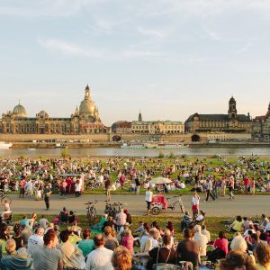 Crowds enjoying an outdoor event along the Elbe River with Dresden's historic skyline in the background.