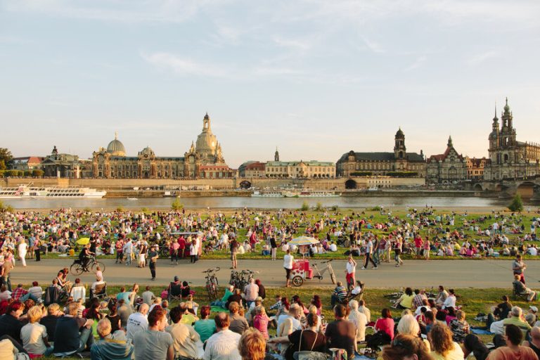 Crowds enjoying an outdoor event along the Elbe River with Dresden's historic skyline in the background.