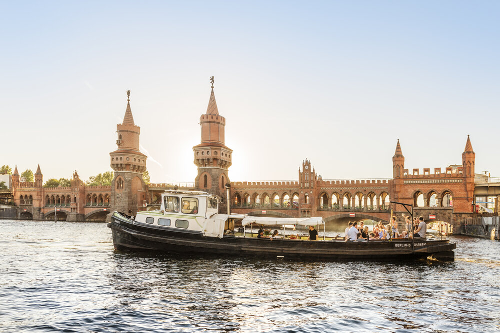 Boat cruising near the iconic Oberbaum Bridge in Berlin at sunset, showcasing the city's rich architecture and vibrant atmosphere.
