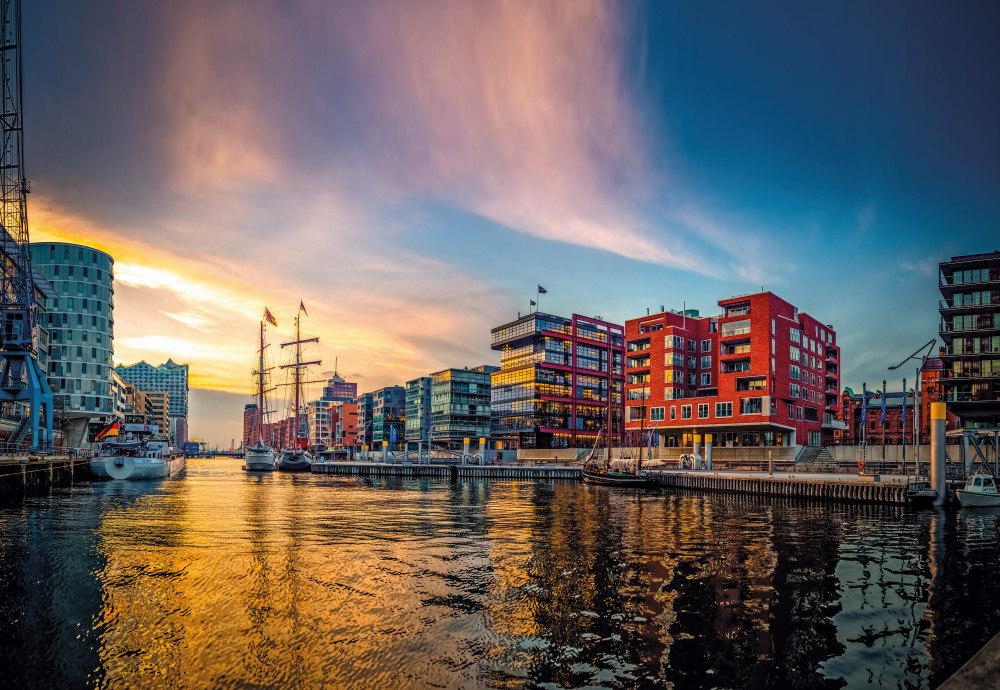 Modern buildings along the Sandtorhafen in Hamburg's HafenCity, featuring colorful facades and docked boats at sunset.