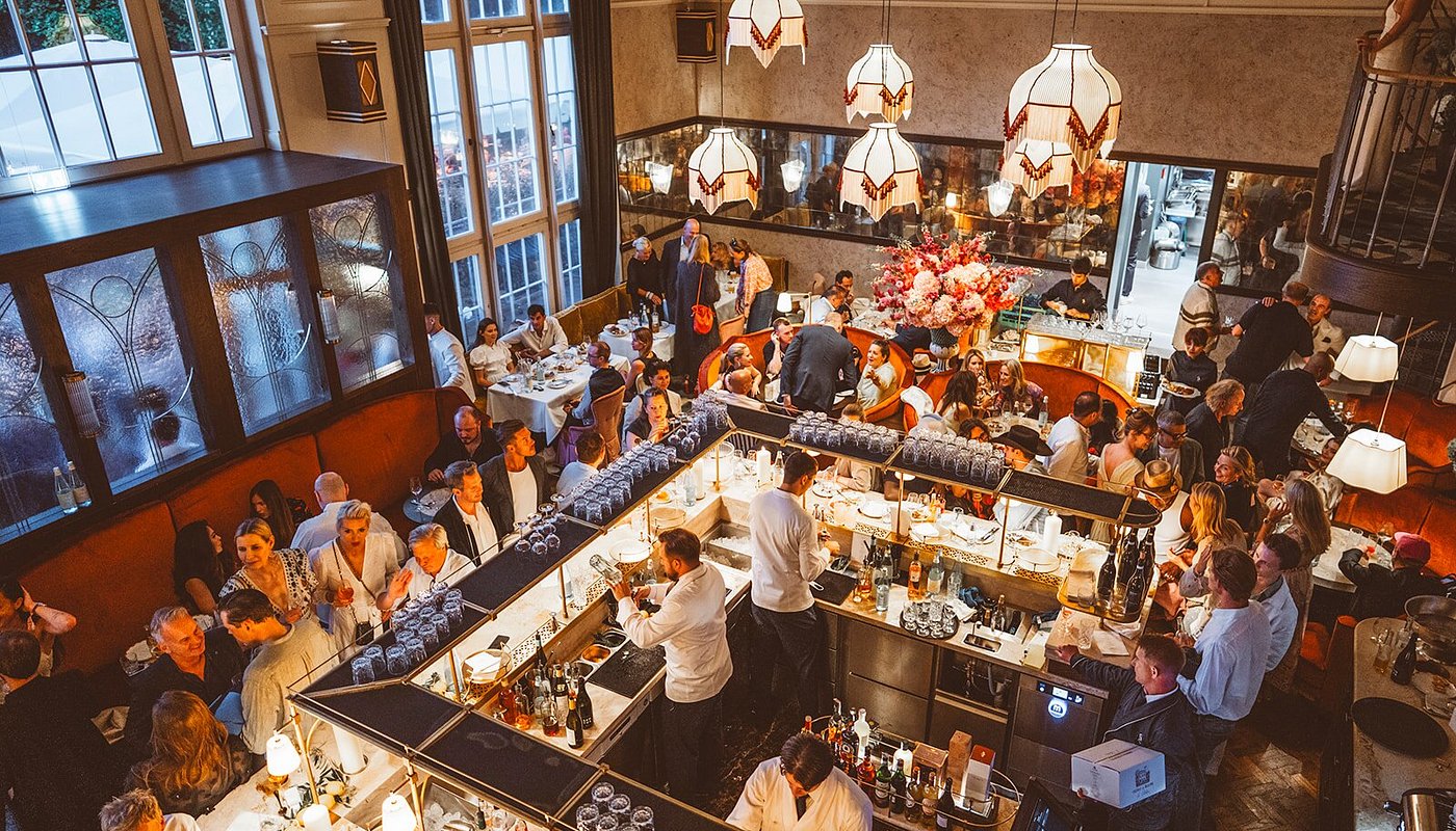 A bustling restaurant interior with patrons dining and enjoying drinks, featuring elegant decor and ambient lighting.