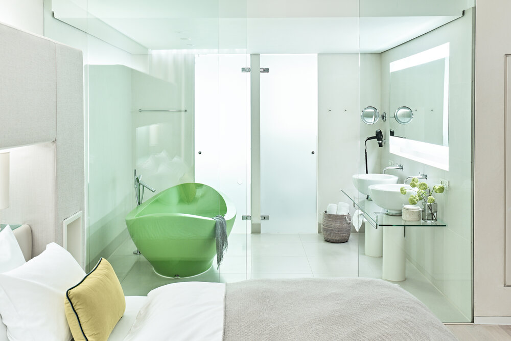 Modern bathroom with a green bathtub, dual sinks, and stylish decor, featuring glass walls and ample natural light.