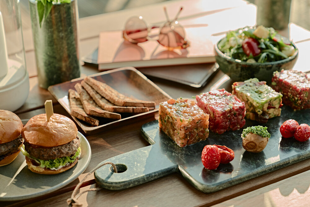 An assortment of gourmet snacks including burgers, crackers, layered salads, and cherry tomatoes on a serving board.