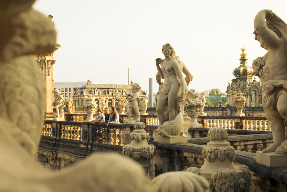 Sculptures and ornate architecture in the Dresden Zwinger, with visitors enjoying the view in the background.