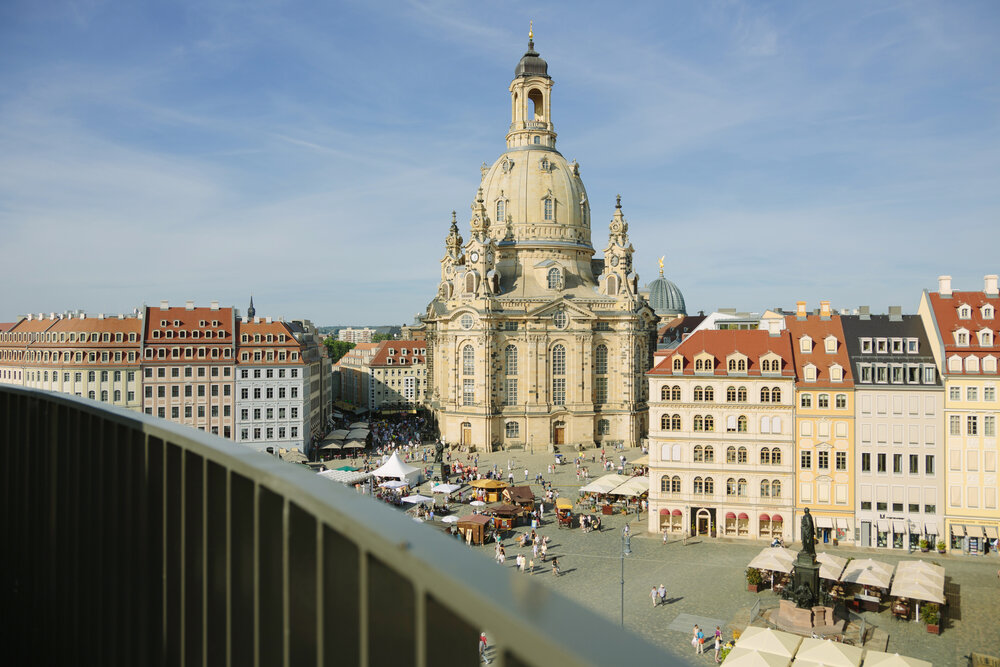 Baroque Frauenkirche with its iconic dome in Dresden, surrounded by historic buildings and a bustling square beneath a clear sky.