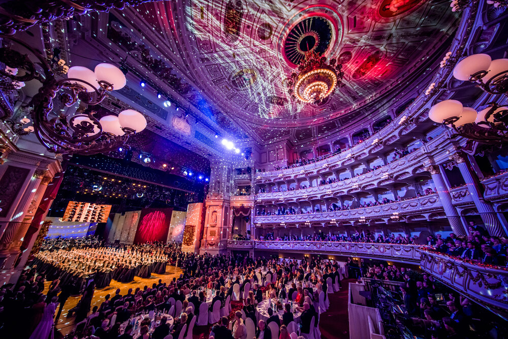 Elegant ballroom scene at the Semperoper in Dresden during a gala event, showcasing ornate architecture and a dazzling chandelier.