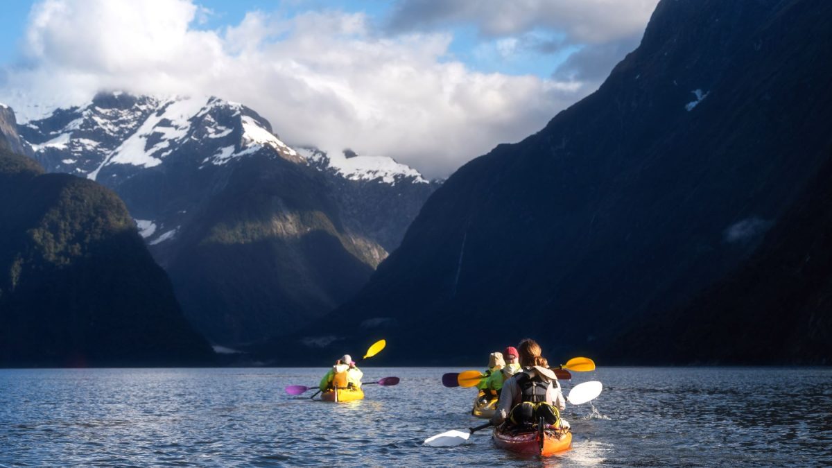 Kayakers paddle through calm waters surrounded by majestic mountains in New Zealand's South Island.
