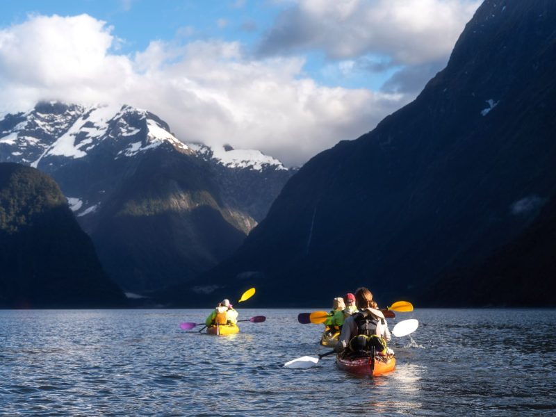 Kayakers paddle through calm waters surrounded by majestic mountains in New Zealand's South Island.