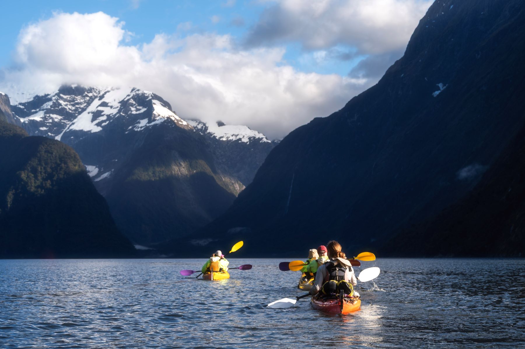 Kayakers paddle through calm waters surrounded by majestic mountains in New Zealand's South Island.