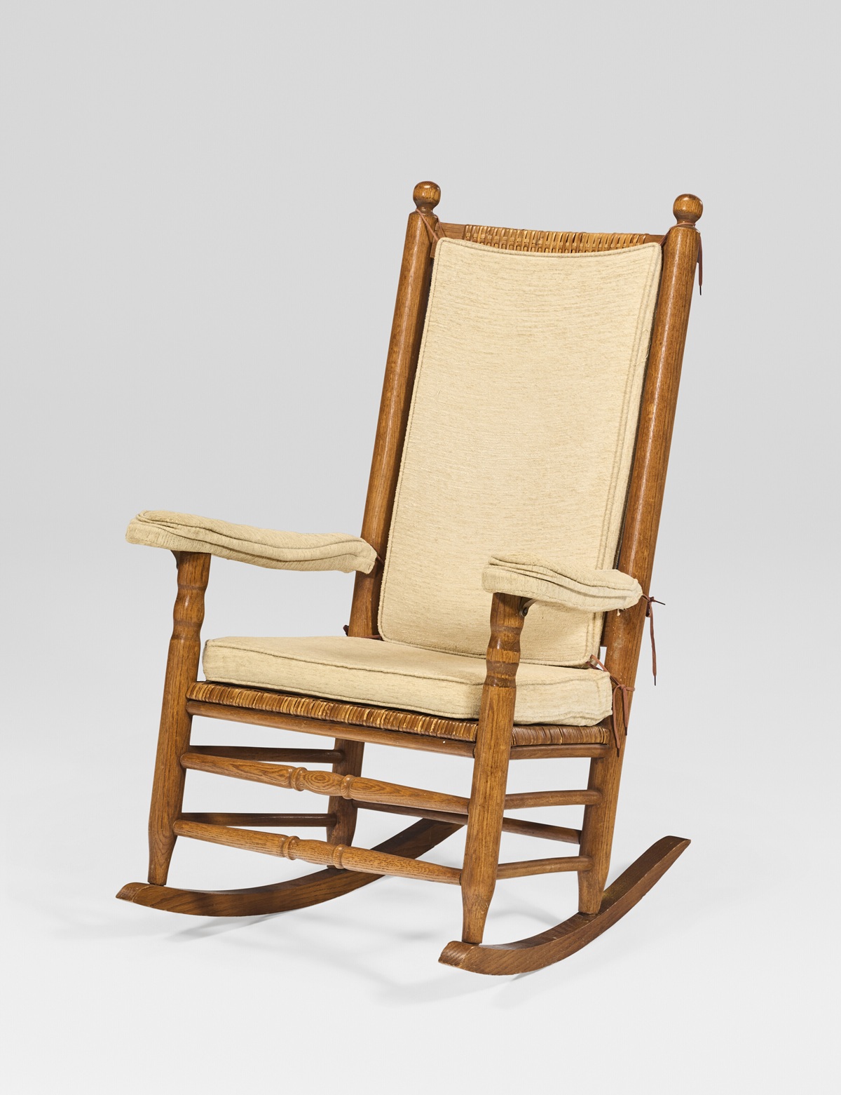 A vintage wooden rocking chair with soft beige upholstery, part of the Jim Irsay Collection auction at Christie's New York.