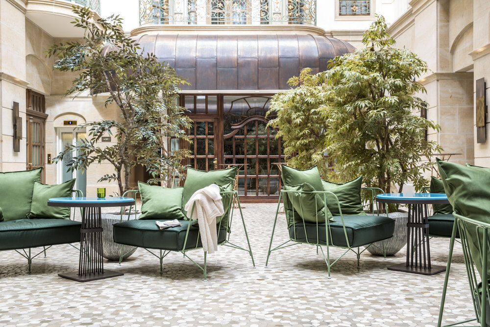 Stylish seating area with green cushions and tables surrounded by plants in a bright atrium space.