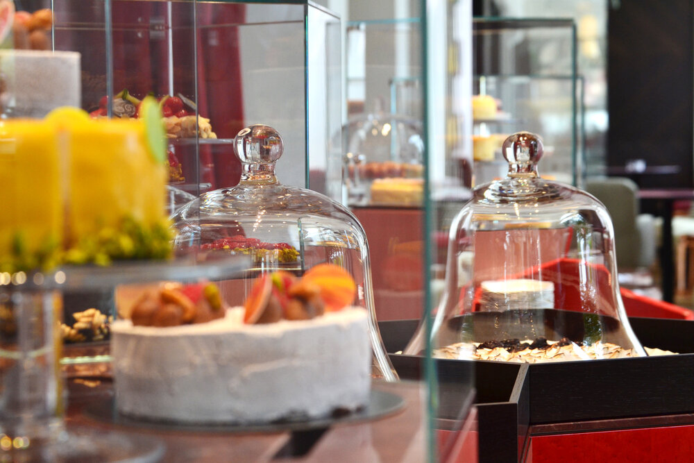 Delicious cakes and desserts displayed under glass domes in a stylish bakery setting.