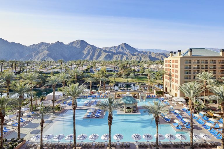 Resort pool area at Renaissance Esmeralda with palm trees, lounge chairs, and mountains in the background under a clear sky.