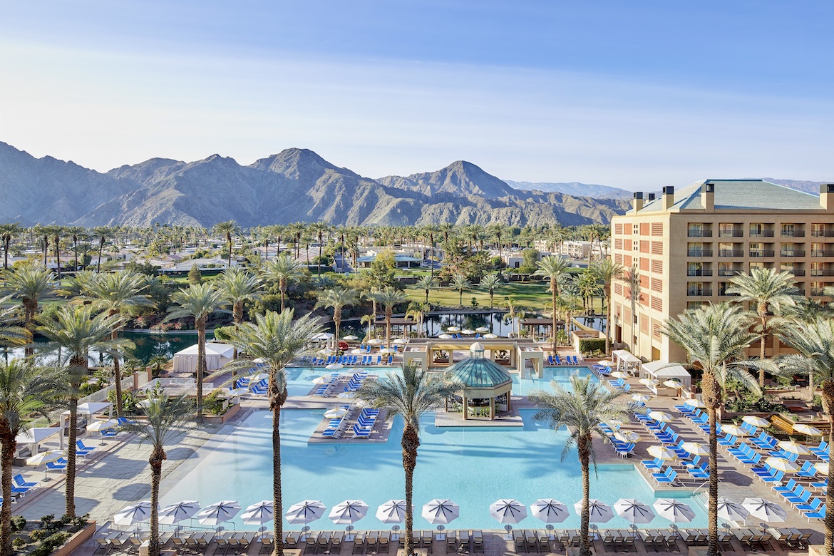 Resort pool area at Renaissance Esmeralda with palm trees, lounge chairs, and mountains in the background under a clear sky.