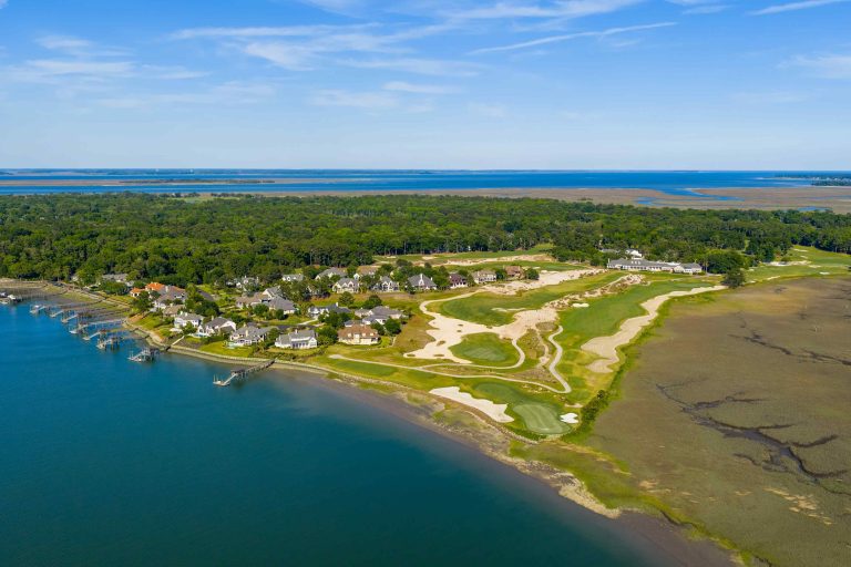 Aerial view of luxury homes and a golf course along the Colleton River in Bluffton, showcasing lush greenery and waterfront.