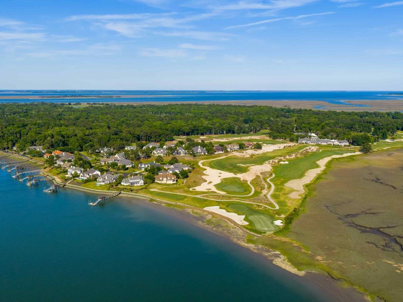 Aerial view of luxury homes and a golf course along the Colleton River in Bluffton, showcasing lush greenery and waterfront.