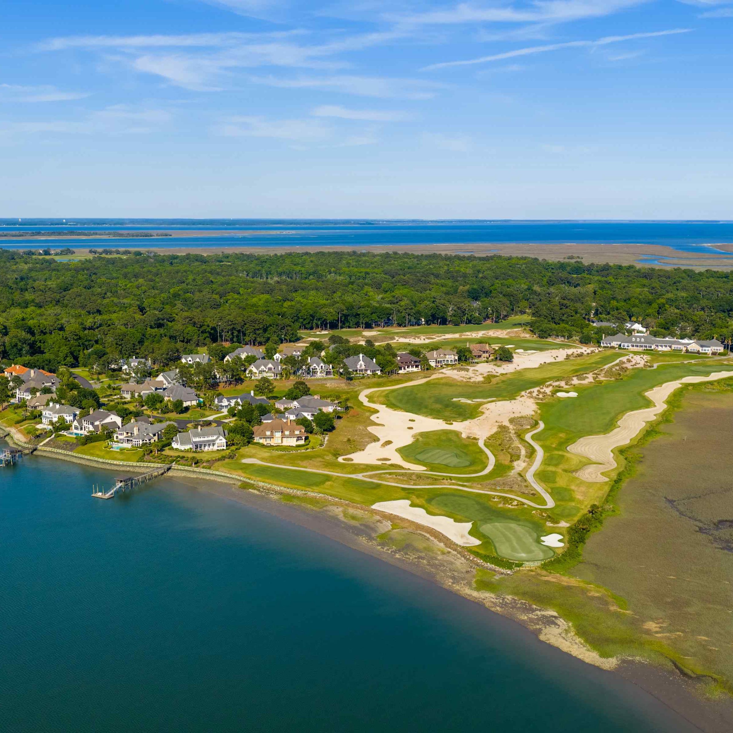 Aerial view of luxury homes and a golf course along the Colleton River in Bluffton, showcasing lush greenery and waterfront.