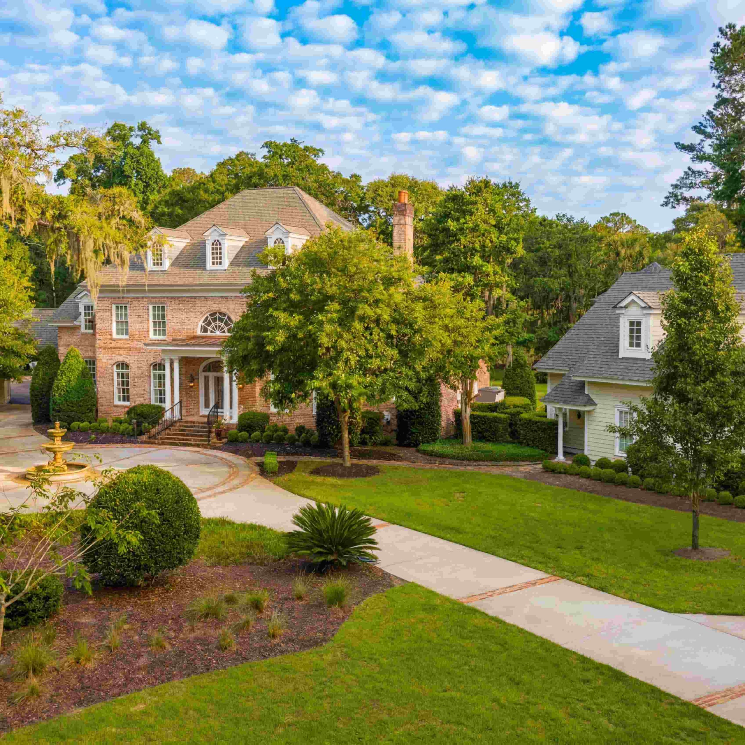 Luxurious brick estate surrounded by lush greenery, with a circular driveway and fountain, in Bluffton's Colleton River.