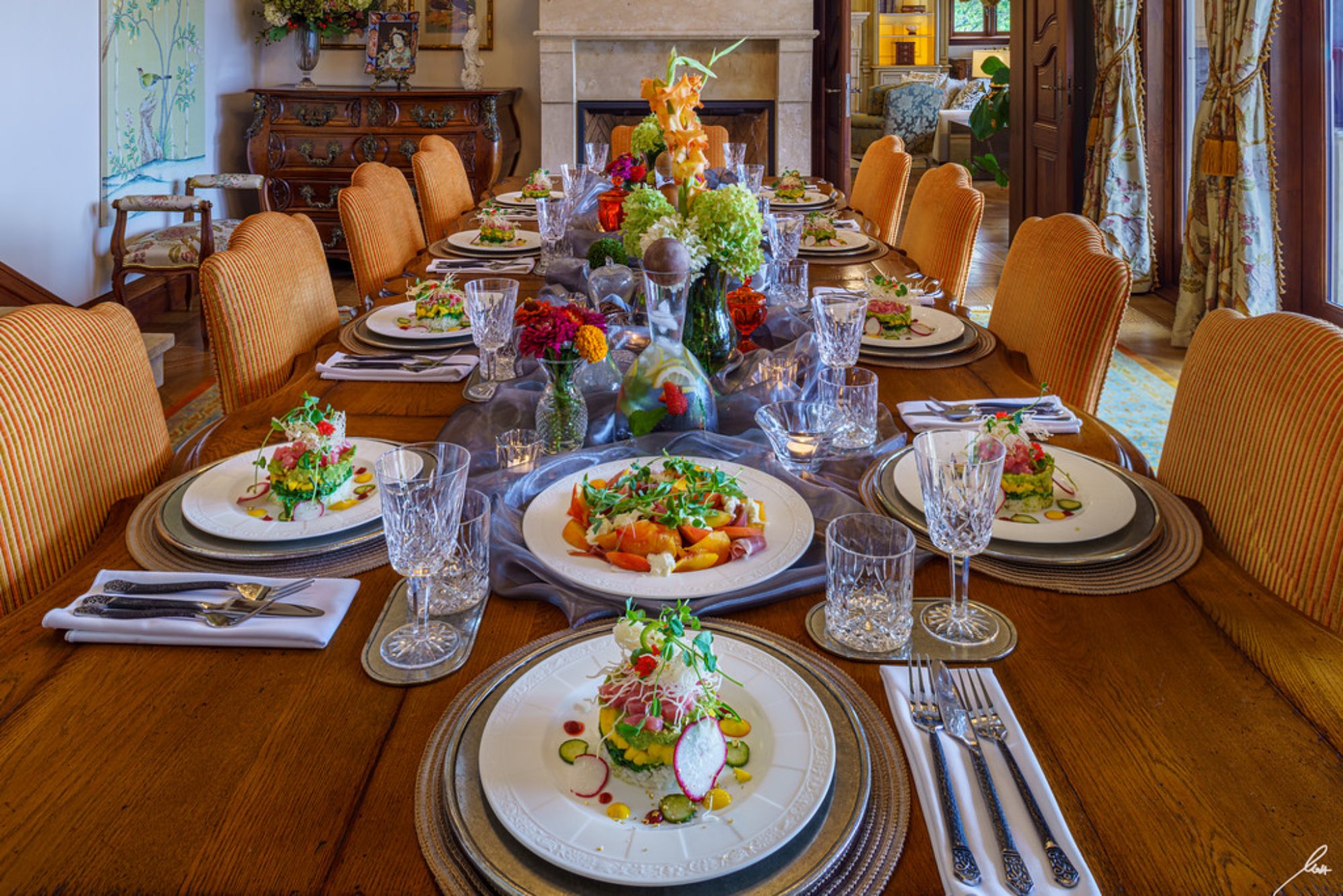 An elegantly set dining table featuring gourmet dishes, crystal glassware, and floral decor in a luxurious waterfront estate.