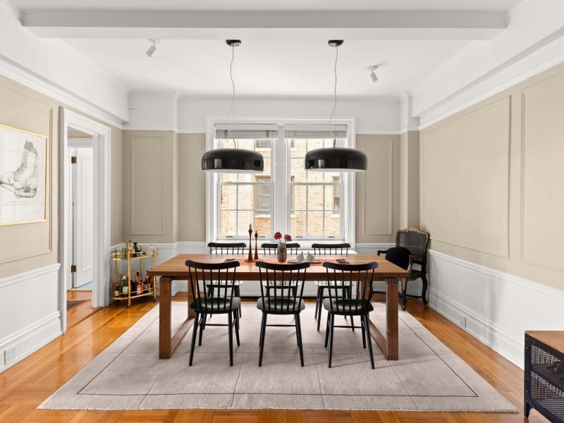 Modern dining area featuring a wooden table, black chairs, and elegant light fixtures against a soft color palette.