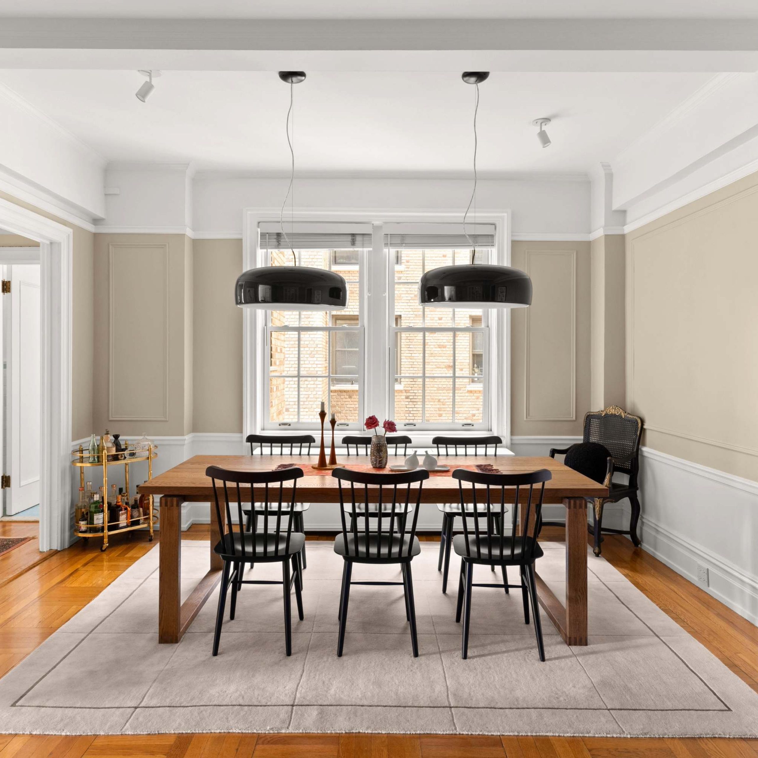 Modern dining area featuring a wooden table, black chairs, and elegant light fixtures against a soft color palette.