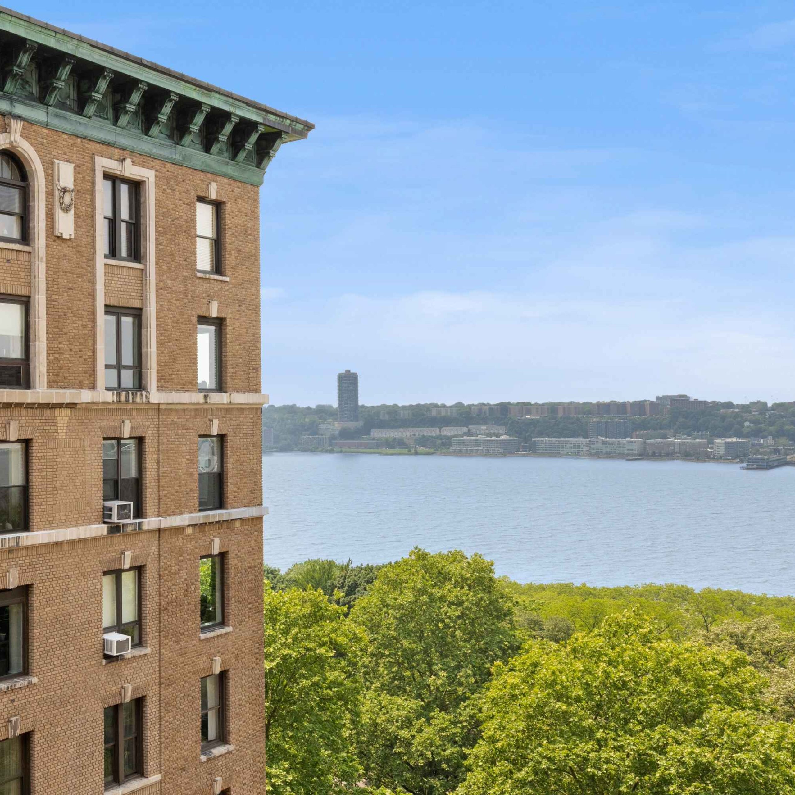 Historic brick co-op building with lush trees along the waterfront, showcasing views of the river and city skyline.