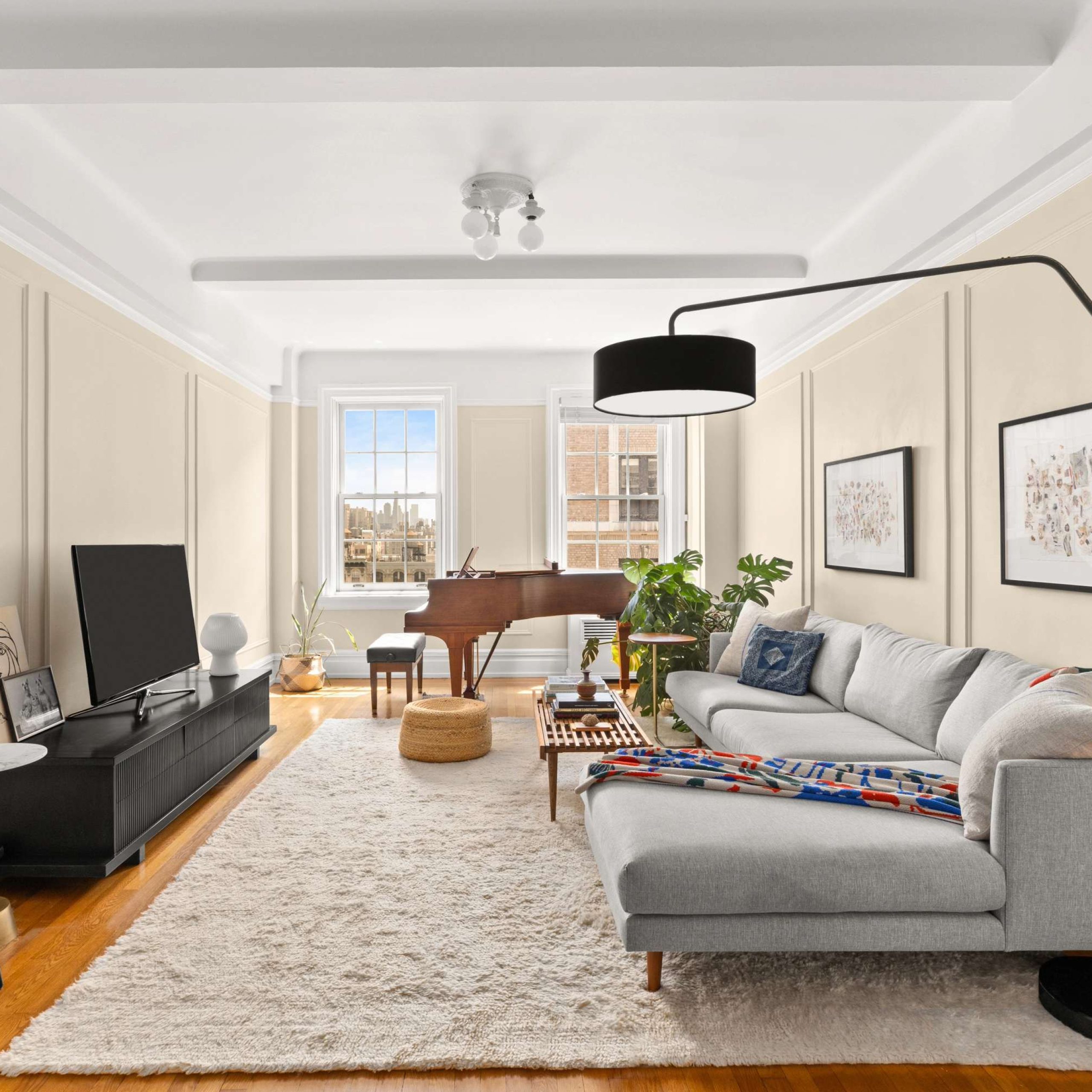 Stylish living room featuring a gray sectional sofa, piano, and modern decor, with large windows providing natural light.