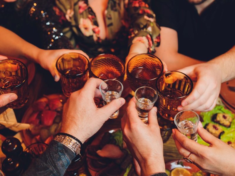 Hands clinking glasses in a toast, surrounded by food and drinks, capturing a lively bachelor party celebration.