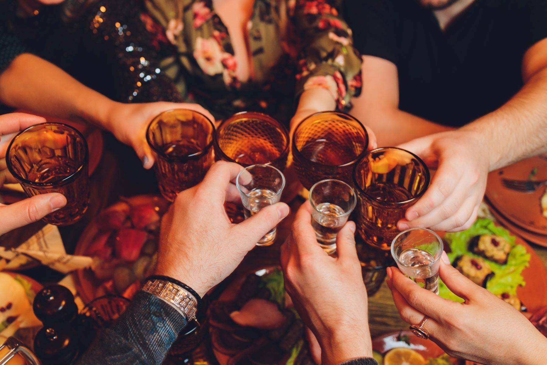 Hands clinking glasses in a toast, surrounded by food and drinks, capturing a lively bachelor party celebration.