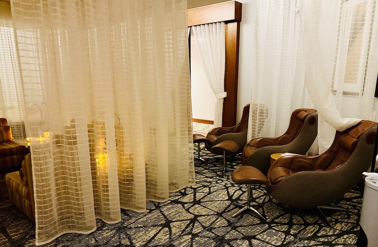 Cozy relaxation lounge featuring comfortable chairs, soft lighting, and sheer curtains, perfect for wellness treatments.