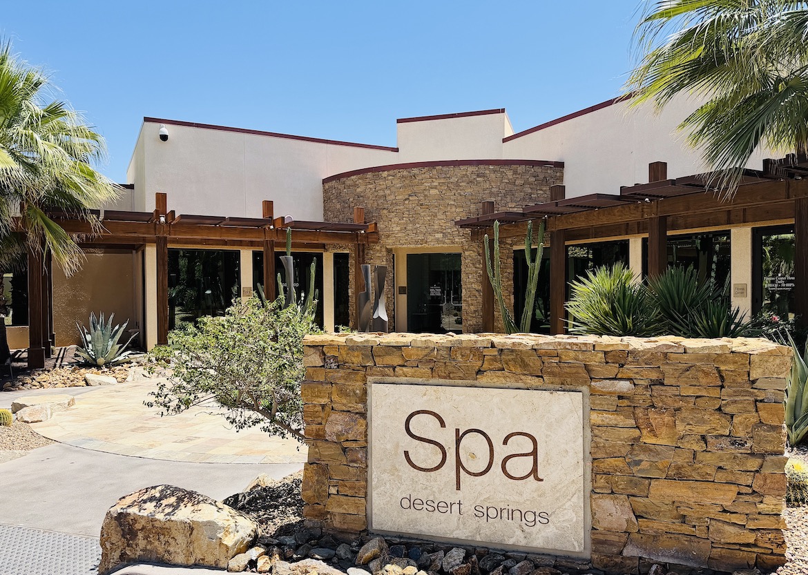 Spa Desert Springs entrance featuring a modern design with natural stone, surrounded by palm trees and desert landscaping.