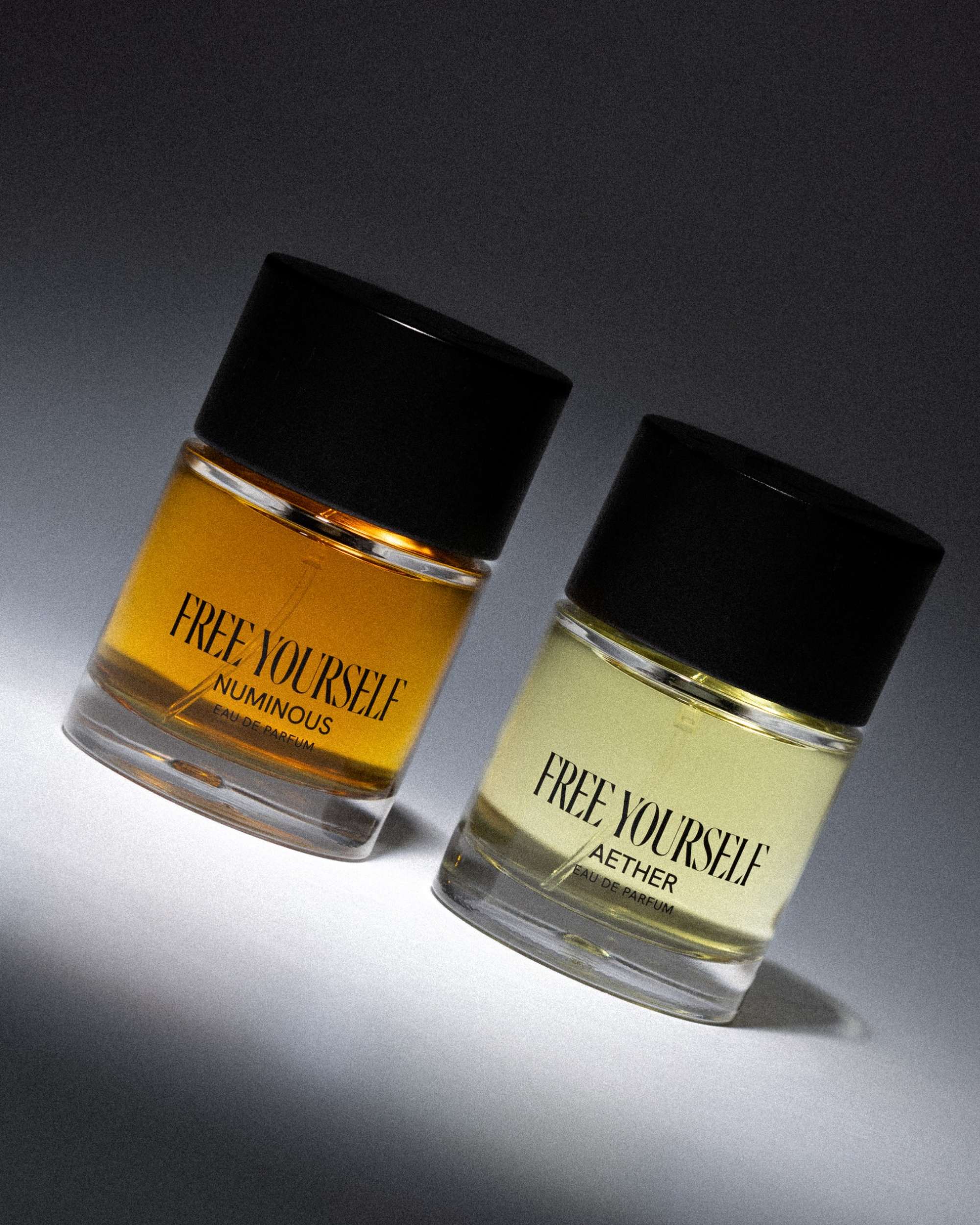 Two perfume bottles labeled "Free Yourself" in black caps, showcasing the scents Numinous and Aether on a gradient background.