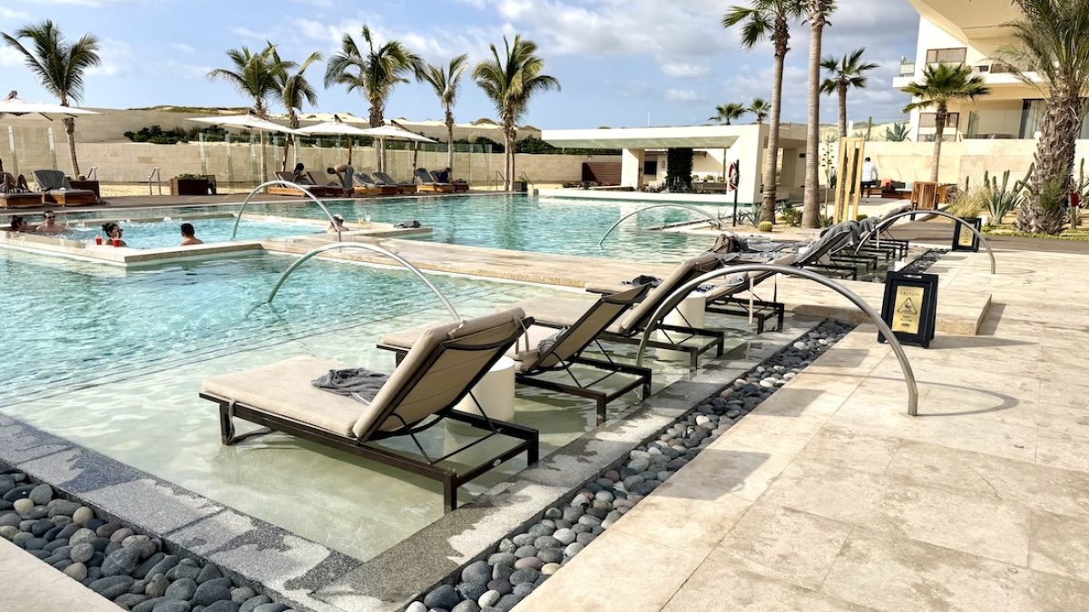 Luxurious pool area at Nobu Hotel & Residence Los Cabos, featuring loungers, palm trees, and guests enjoying the water.
