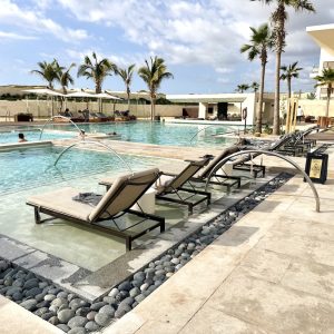 Luxurious pool area at Nobu Hotel & Residence Los Cabos, featuring loungers, palm trees, and guests enjoying the water.