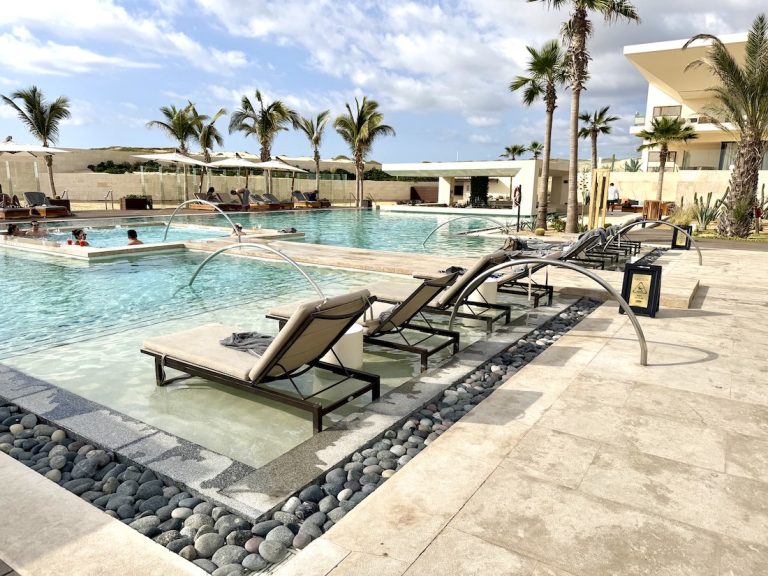 Luxurious pool area at Nobu Hotel & Residence Los Cabos, featuring loungers, palm trees, and guests enjoying the water.