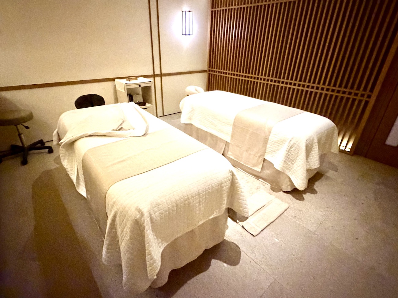 Treatment room with two massage tables, soft lighting, and a calm, minimalistic decor for relaxation and wellness.